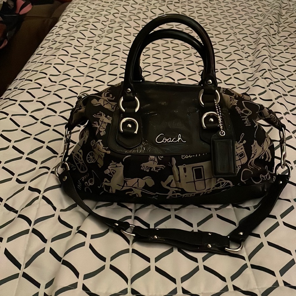 Small to medium black coach bag with beige writing and leather handles.